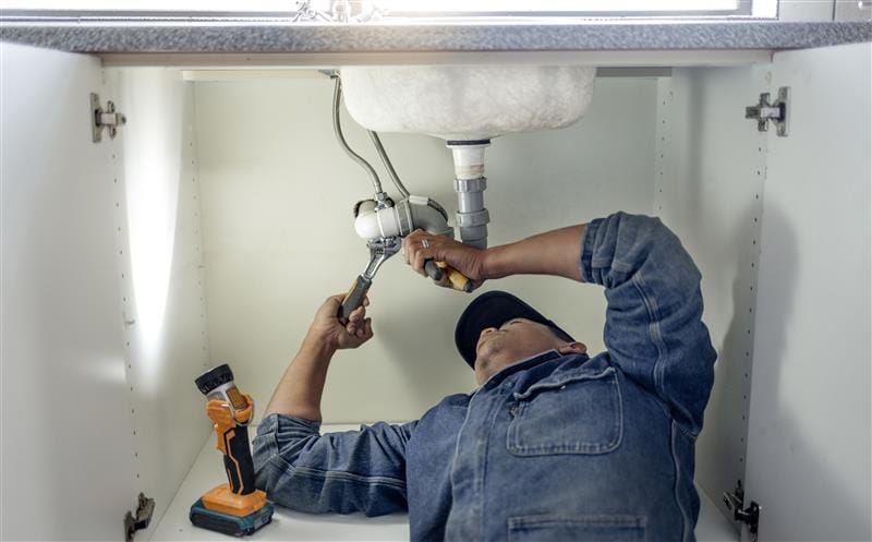 Plumber repairing pipes beneath a bathroom sink in Duluth