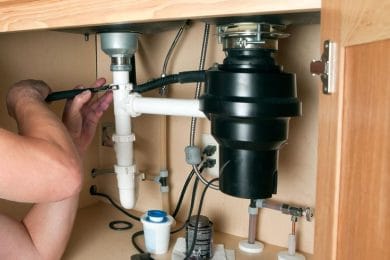 Plumber repairing a garbage disposal beneath a kitchen sink in Duluth