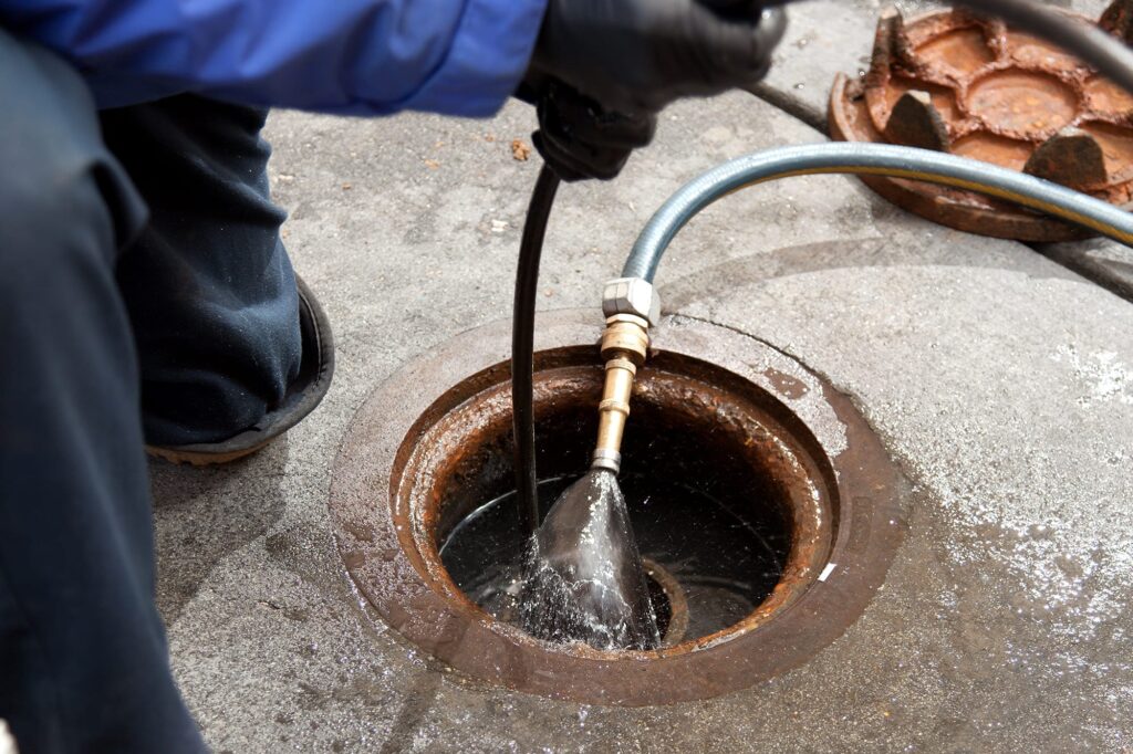 Plumber hydro jetting a sewer line through a manhole in Duluth