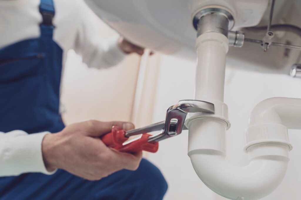 Plumber repairing a white drain pipe beneath a sink in Duluth